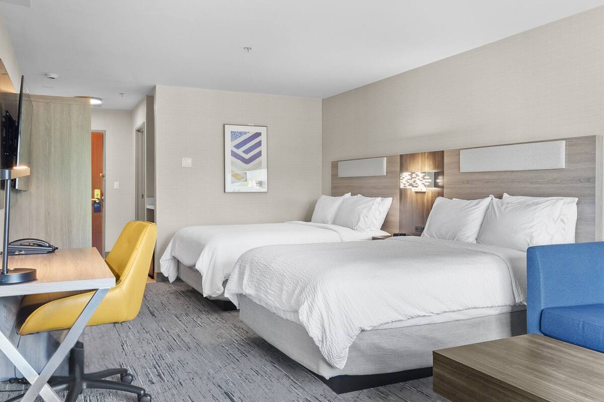 A hotel room with two beds, a desk with a chair, a blue sofa, and a small table.