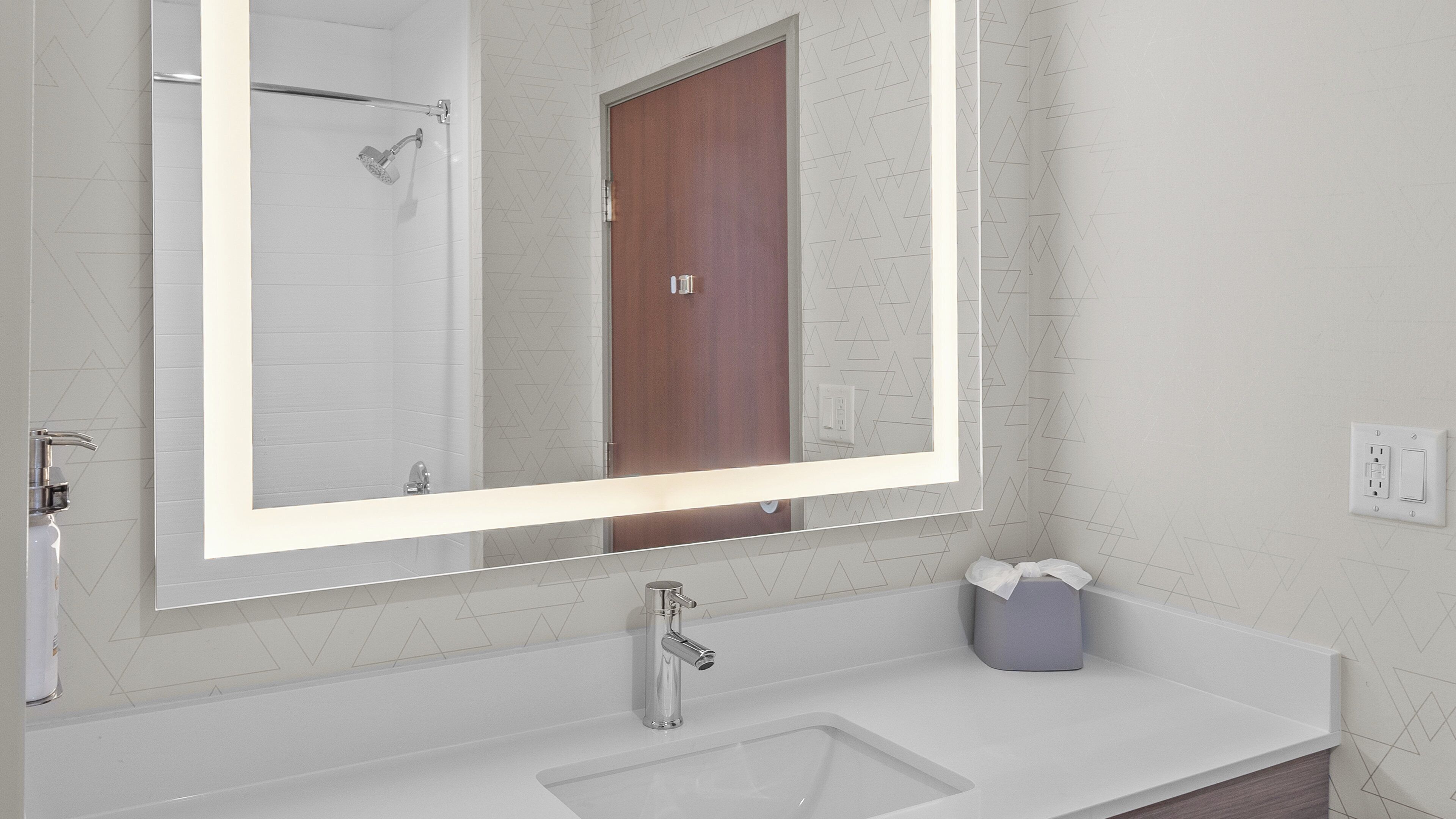 A bathroom with a large mirror, a sink, a shower, and a wooden door.