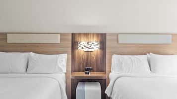 Habitación de hotel con dos camas, cabecero de madera, mesita de noche con un reloj y un pequeño banco.