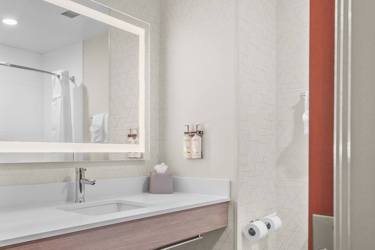 A bathroom with a white sink, a mirror, a towel rack, and a toilet paper holder.