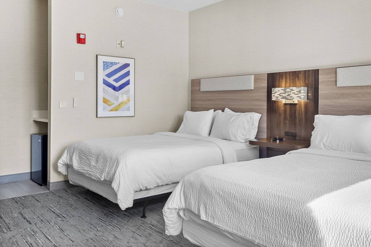 A hotel room with two beds, a wooden headboard, a framed abstract artwork, and a small table with a lamp.