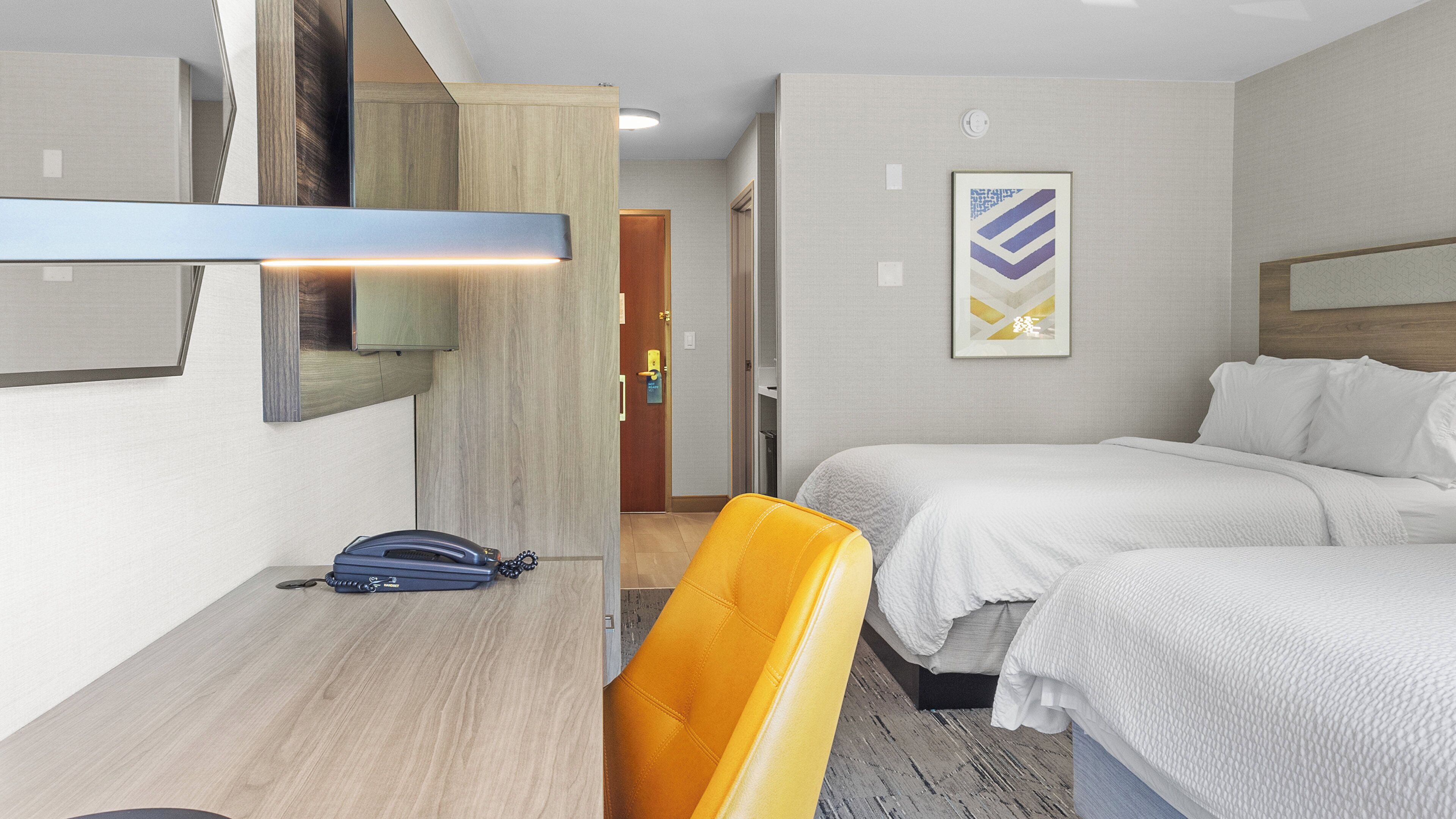 Ein Hotelzimmer mit Bett, Schreibtisch, Stuhl, Telefon und einem Bild an der Wand.