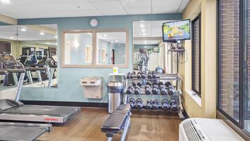 Une salle de sport équipée de tapis de course, d’un banc, d’haltères, d’un miroir et d’un écran de télévision.
