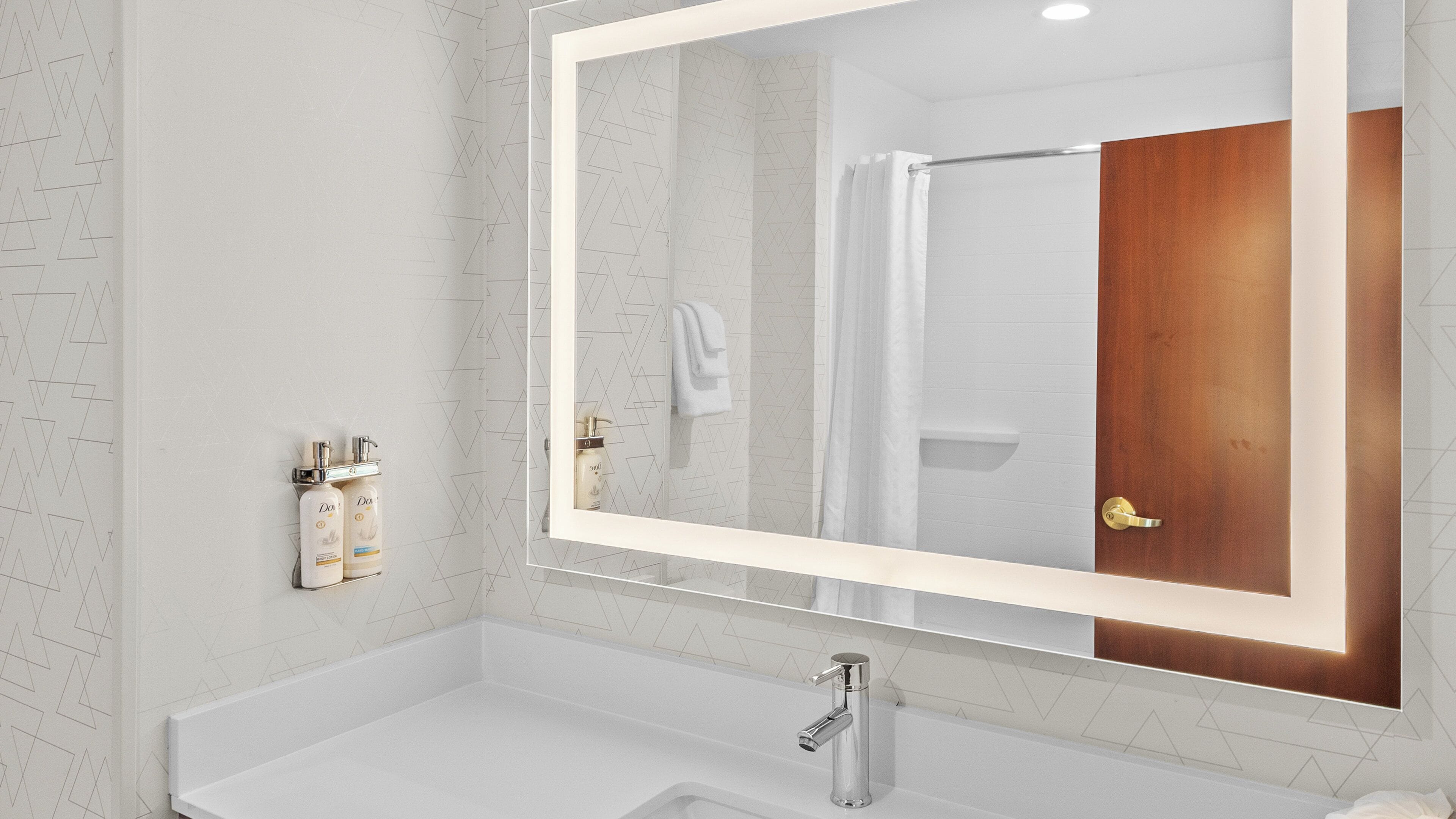 A bathroom with a large mirror, a white sink, and two bottles of Dove soap.