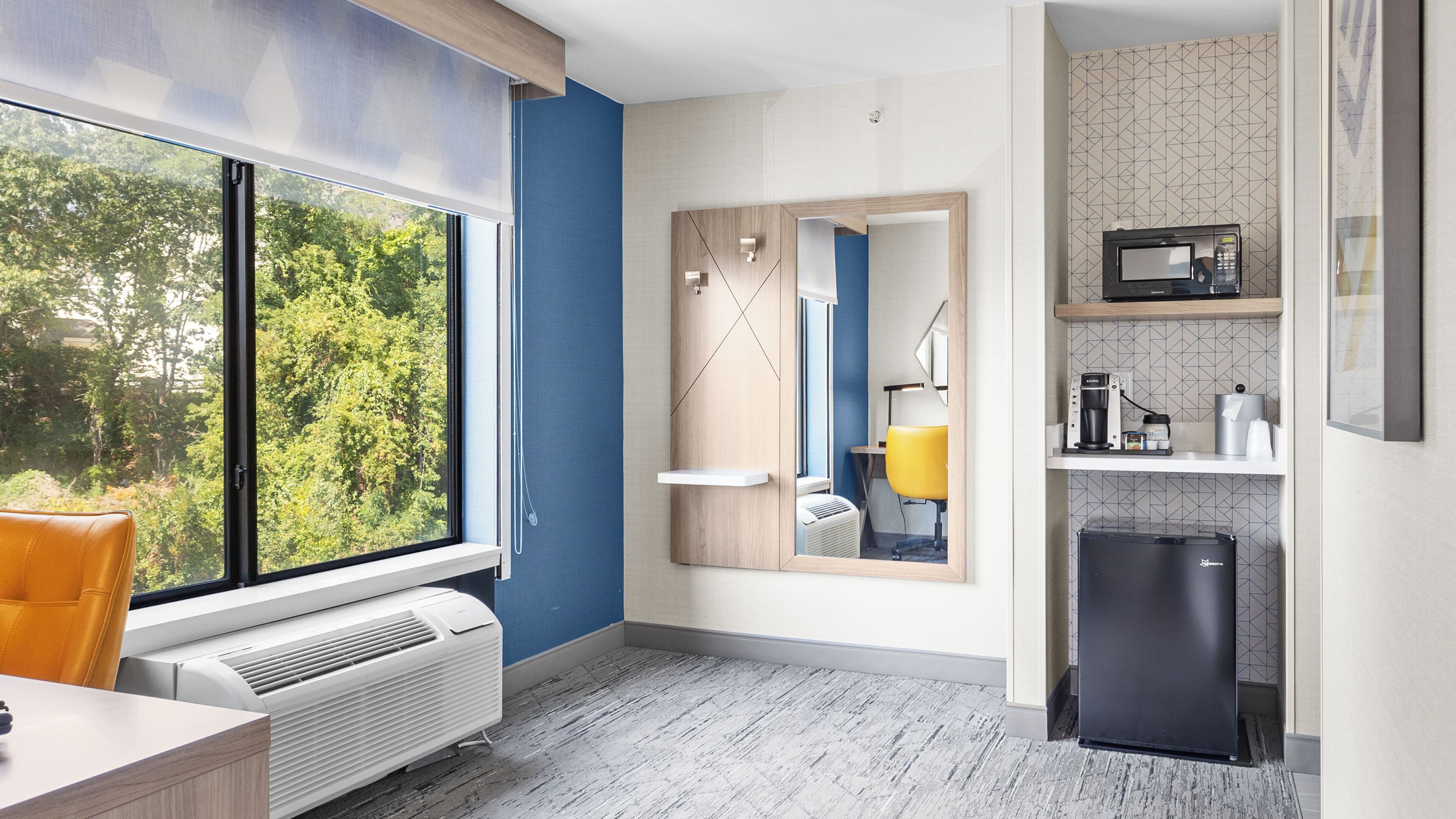 A modern kitchen with a built-in microwave, a small refrigerator, and a window with a view of trees.