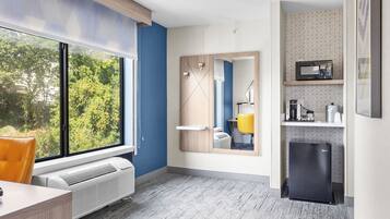 A modern kitchen with a built-in microwave, a small refrigerator, and a window with a view of trees.