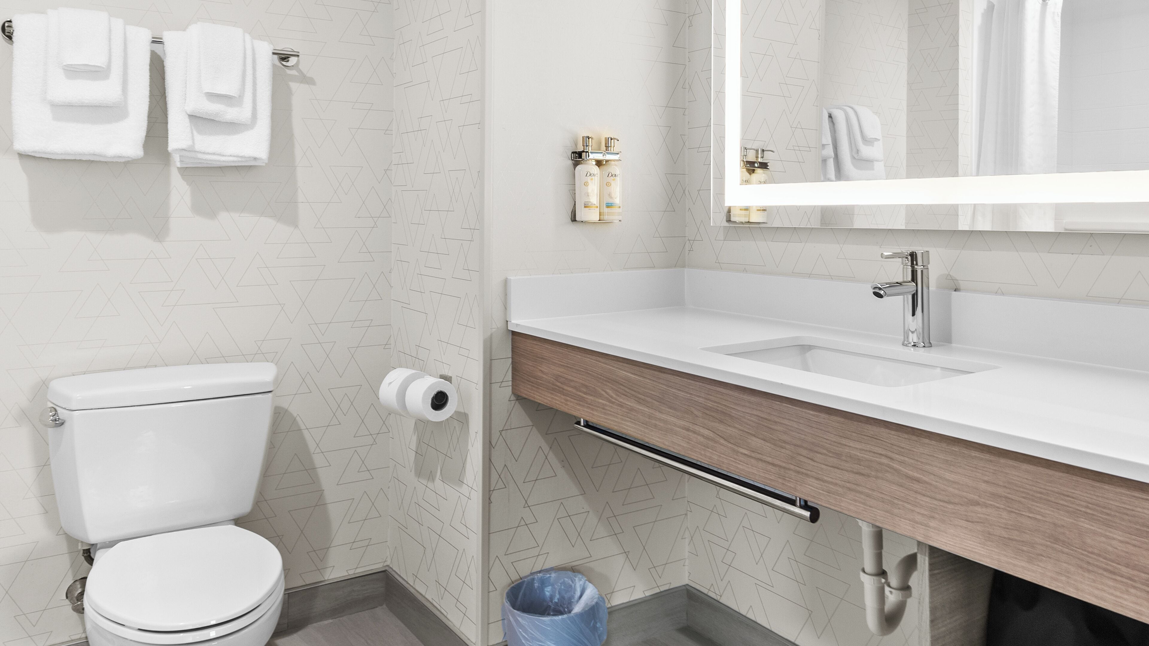 A bathroom with a toilet, sink, mirror, towel rack, and toiletries.