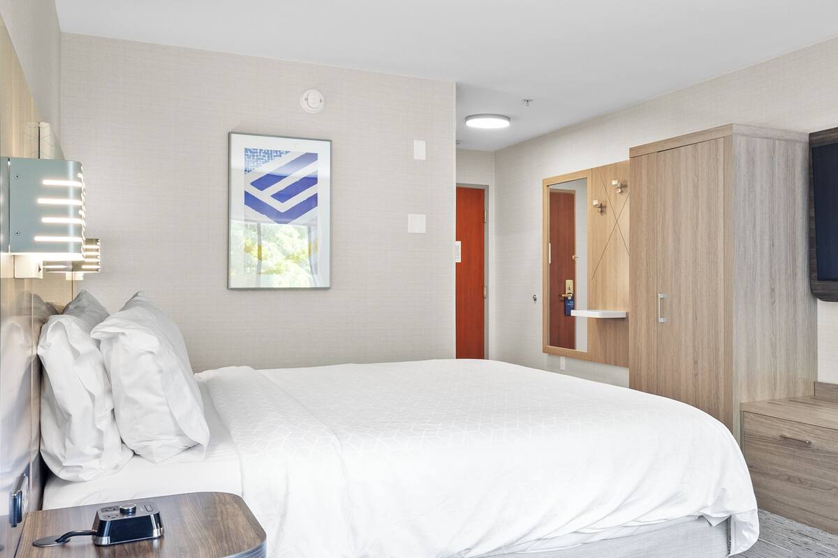 A hotel room with a bed, a desk with a camera, a wardrobe, a TV, and a door.