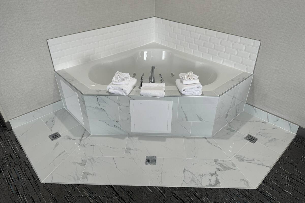 A corner bathroom with a freestanding bathtub, white marble tiles, and a towel rack.