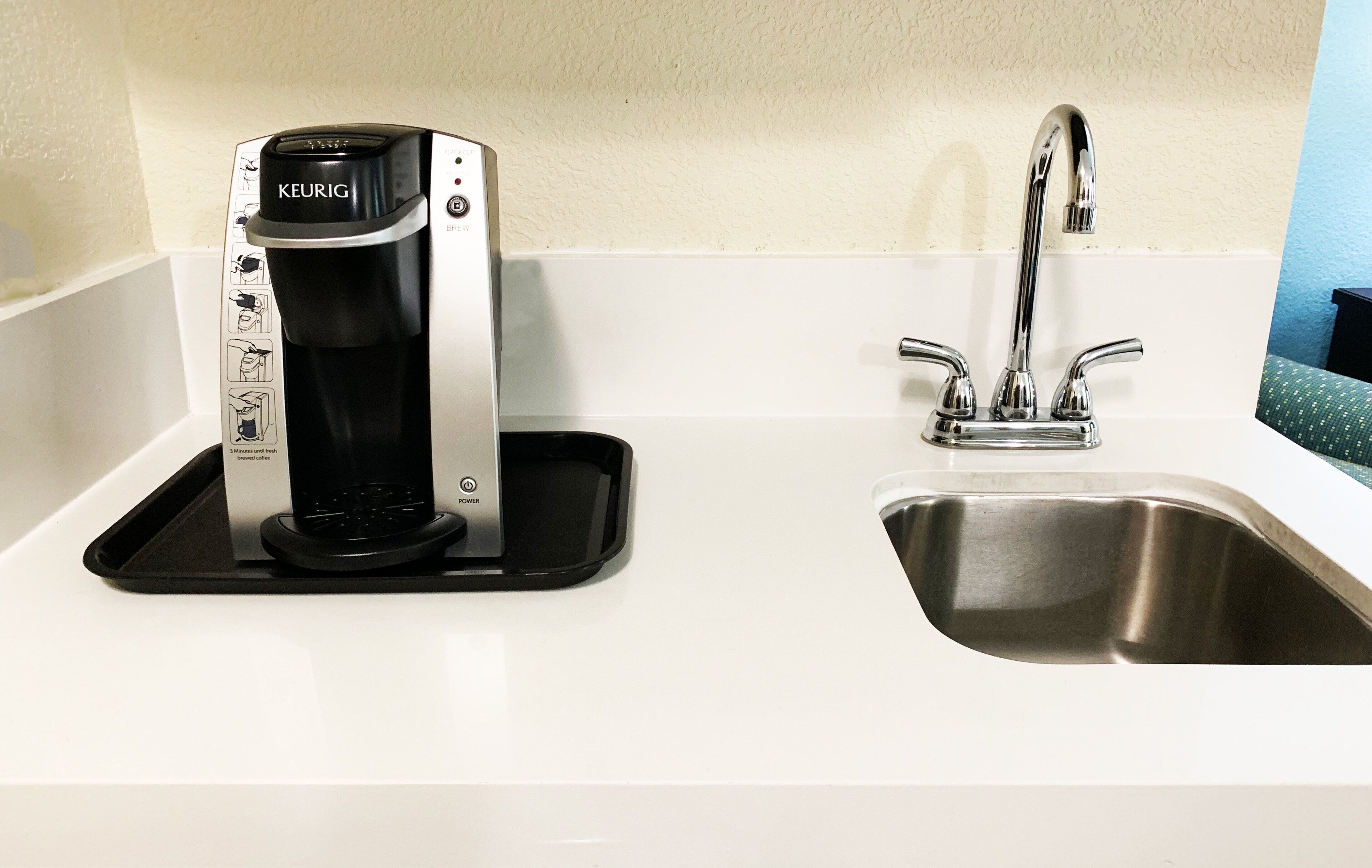 Eine Keurig-Kaffeemaschine steht auf einer weißen Arbeitsplatte neben einem Edelstahl-Spülbecken.