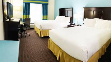 A hotel room with two beds, a desk with a computer, a chair, a nightstand with a lamp, and a window with curtains.