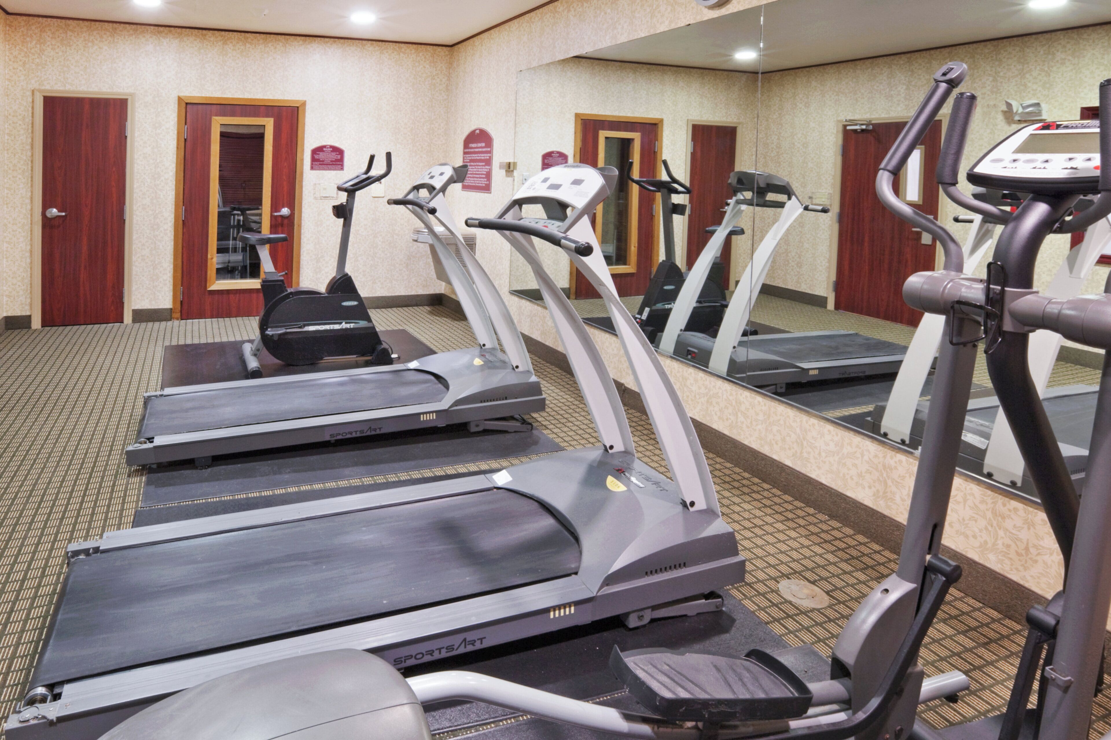 A fitness center with multiple treadmills, a mirrored wall, and a carpeted floor.