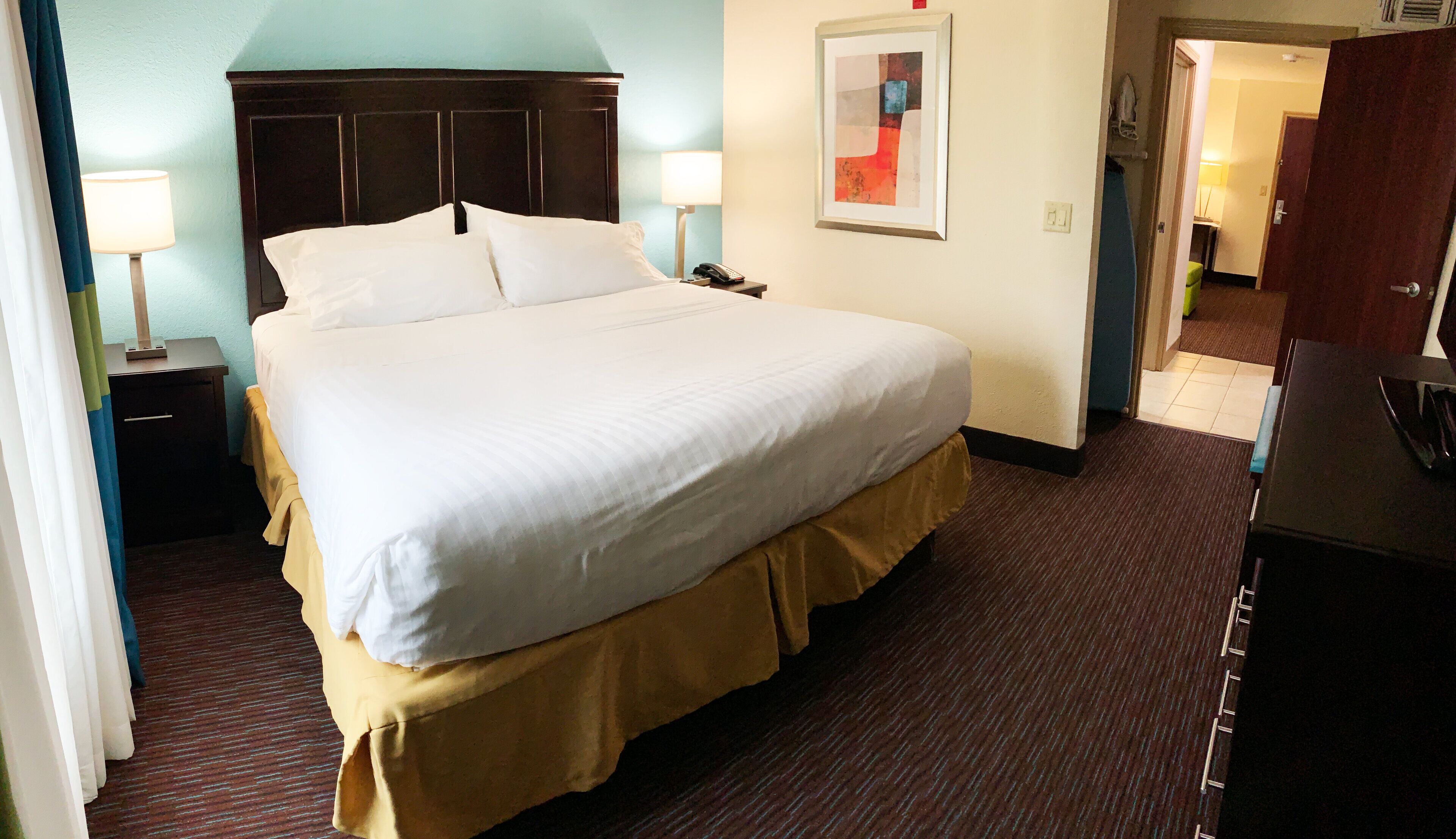 A hotel room with a large bed, bedside lamps, a telephone, and a painting on the wall.