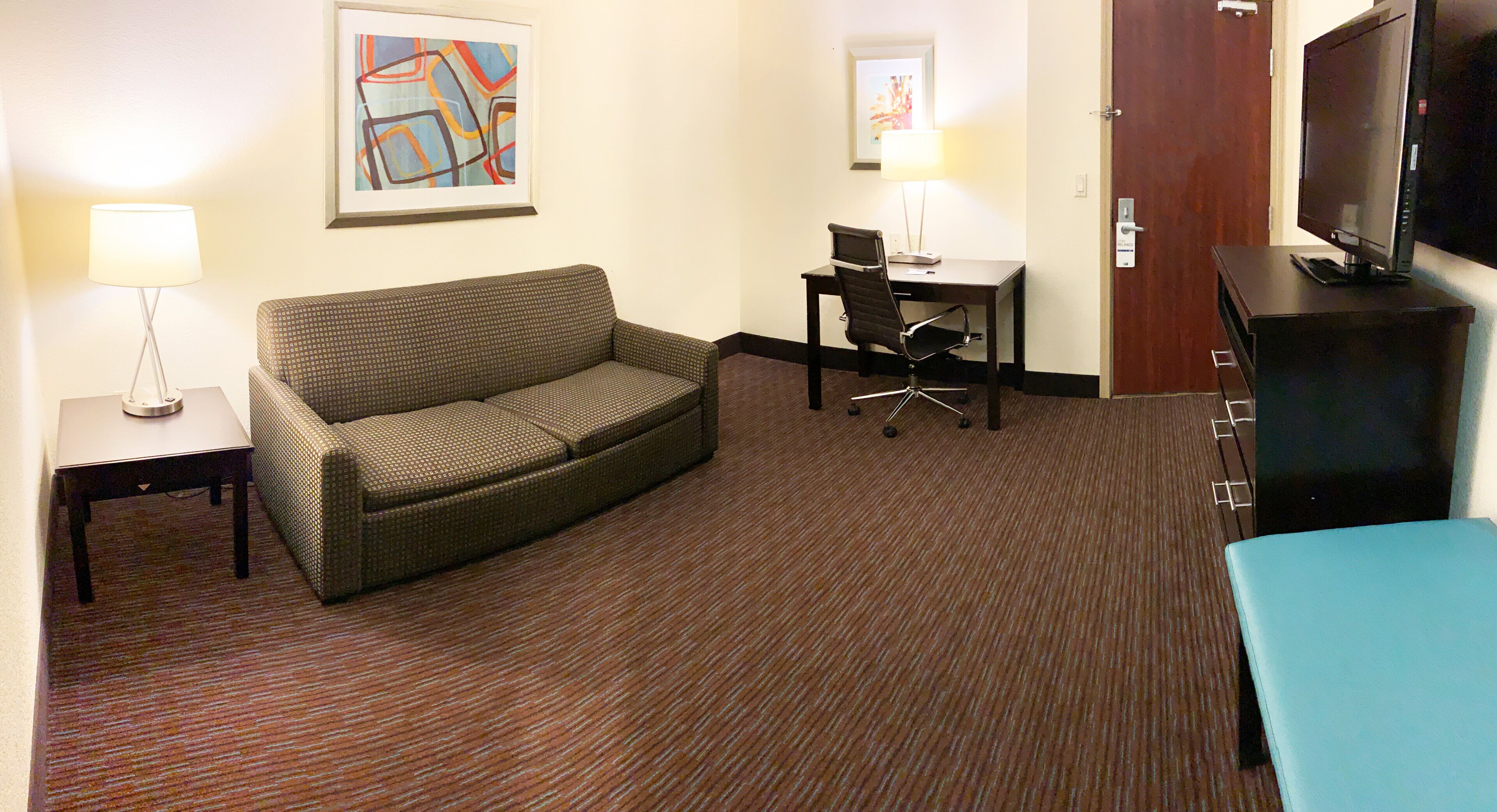 Habitación de hotel con sofá, escritorio, silla, televisor y obras de arte en las paredes.