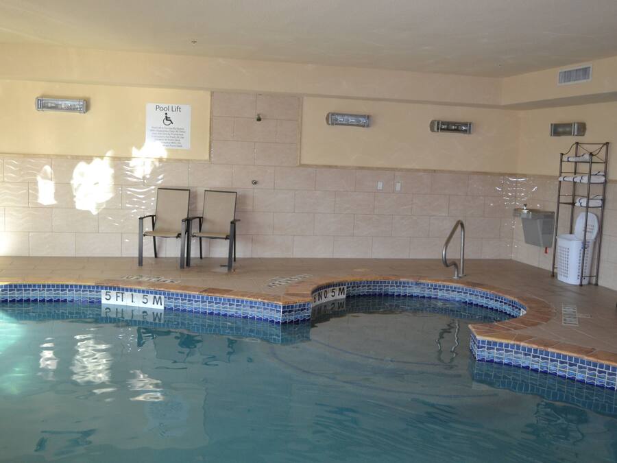 Una piscina interior con borde de azulejos, un elevador de piscina y una silla.