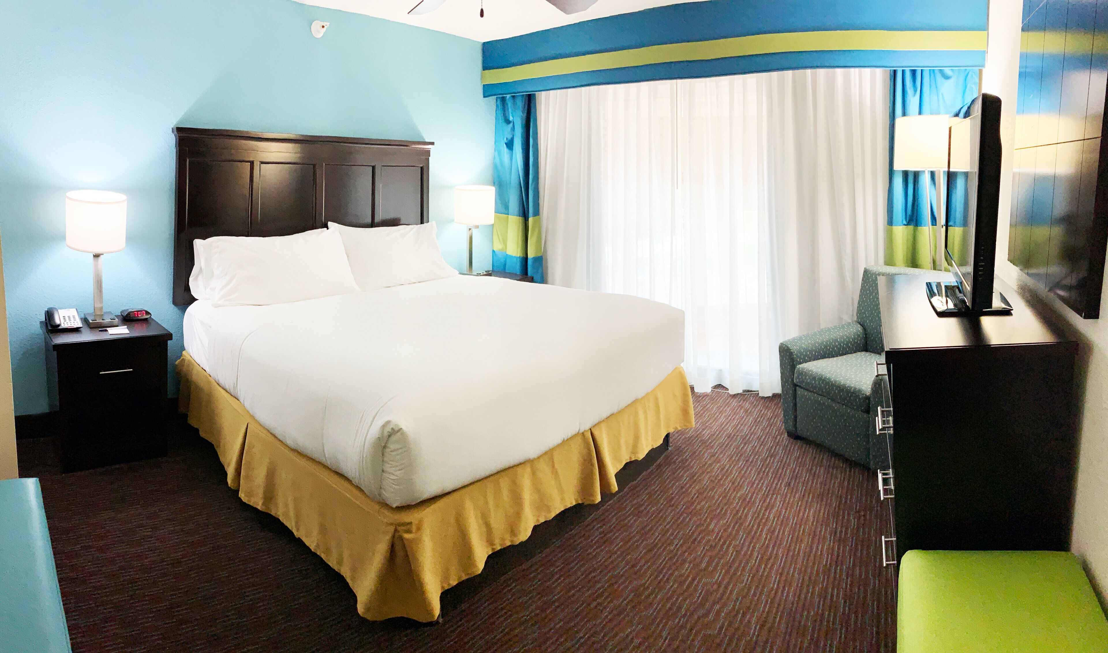 Habitación de hotel con una cama grande, lámparas de noche, un escritorio con teléfono y un televisor sobre un mueble.