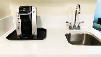 Eine Kaffeemaschine von Keurig auf einer schwarzen Ablage neben einer Edelstahlspüle in einer Küche.