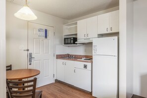 Eine kleine Küche mit weißen Schränken, einer Mikrowelle, einem Kühlschrank und einem Holzespeisetisch mit Stühlen.
