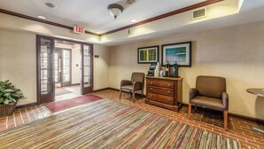 Um saguão de hotel com balcão de recepção, duas poltronas, um espaço de café e sinalização de saída.