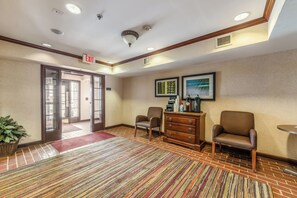 Un hall d’hôtel comprenant un comptoir d’accueil, deux fauteuils, un coin café et un panneau indiquant la sortie.