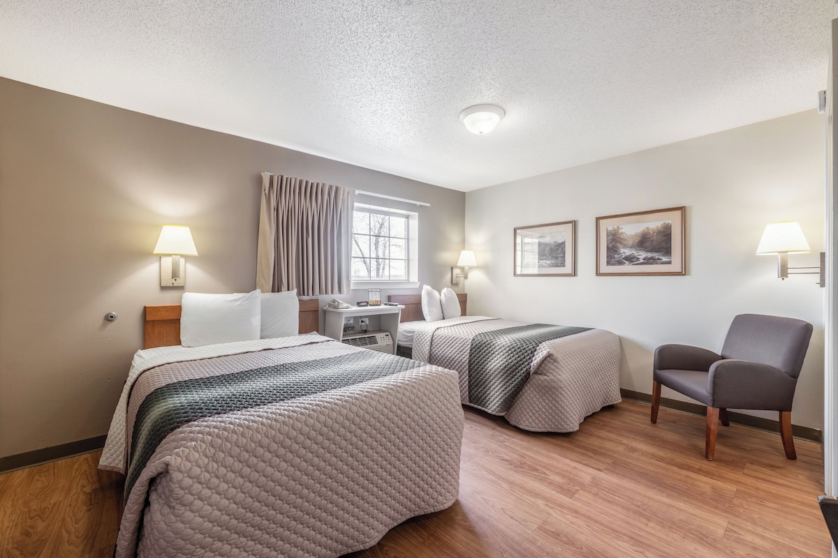 Habitación de hotel con dos camas, un escritorio, una silla y dos lámparas fijadas a la pared.