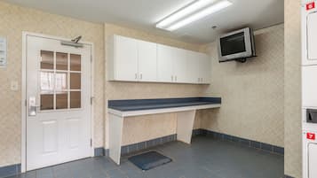 Una cocina limpia y bien iluminada con armarios blancos, un microondas integrado y un televisor pequeño montado en la pared.