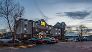 Hotel com fachada de tijolos, várias janelas e estacionamento com diversos carros.
