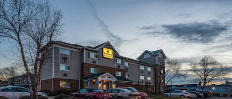 A hotel with a brick facade, multiple windows, and a parking lot with several cars.
