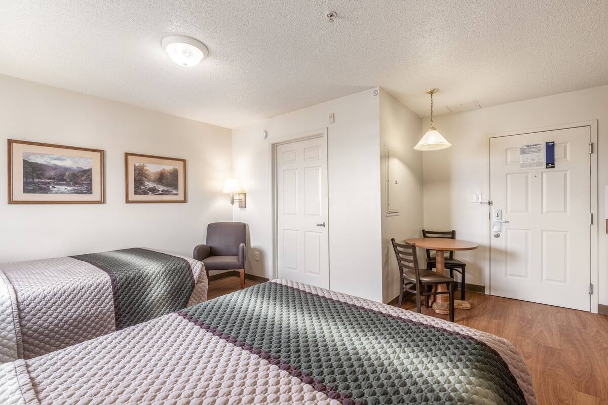 Une chambre avec deux lits, un bureau et une chaise. Deux tableaux encadrés sont accrochés au mur.
