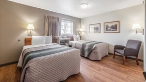 Ett hotellrum med två sängar, ett skrivbord, en stol och ett fönster med gardiner.