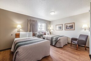 Ein Hotelzimmer mit zwei Betten, einem Schreibtisch, einem Stuhl und einem fensterbepflanzten Fenster.