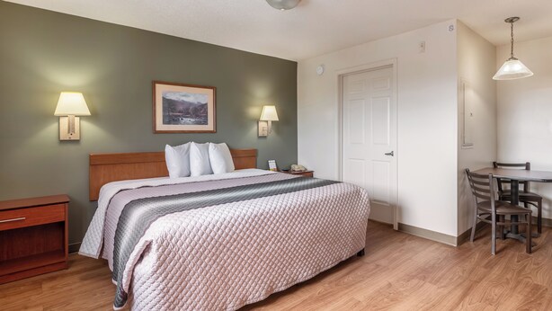 Hotelkamer met een bed, bedlampen, een ingelijst beeld, een deur en een zithoek met een tafel en stoelen.