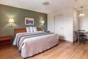 A hotel room with a bed, bedside lamps, a framed picture, a door, and a dining area with a table and chairs.