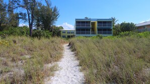A sandy path leading to a building with a green roof and a yellow facade. - Cabana Beach Club by RVA (Longboat Key)