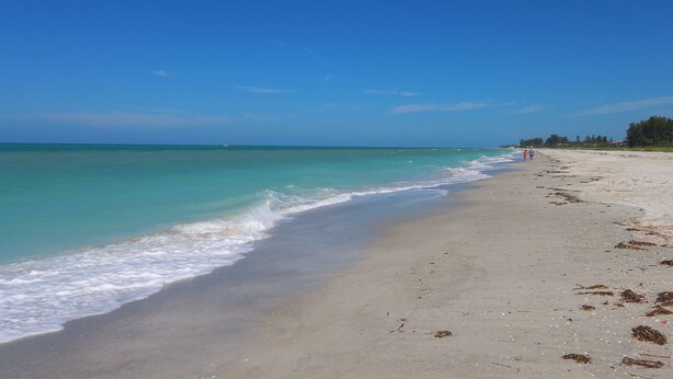 A beach with clear turquoise water, a sandy shore, and a few people in the distance. - Cabana Beach Club by RVA (Longboat Key)