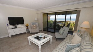 A living room with a television, a sofa, a coffee table, and a balcony with a view of the beach. - Cabana Beach Club by RVA (Longboat Key)