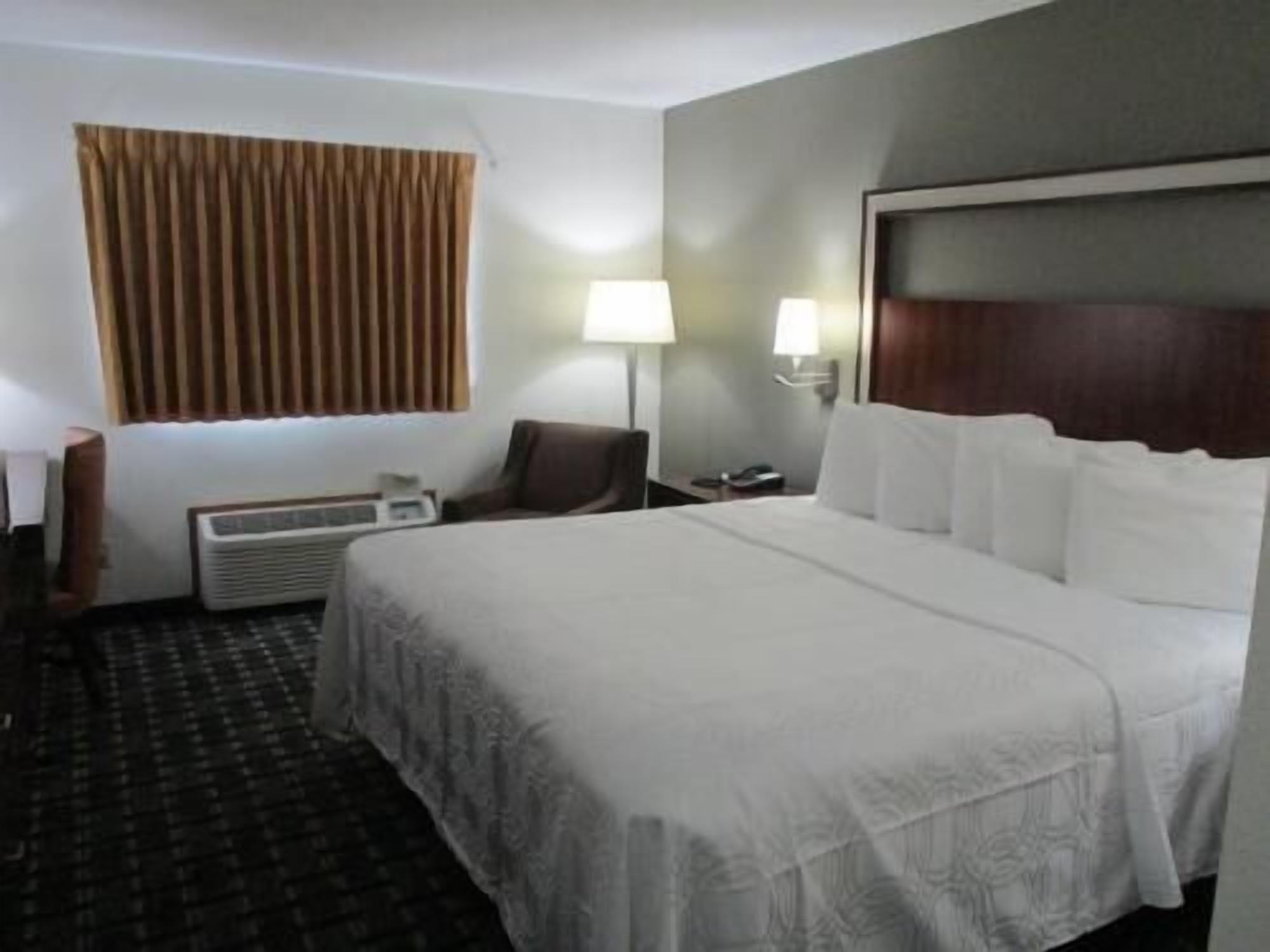 A hotel room with a bed, two bedside lamps, a chair, a desk, and a window with curtains.