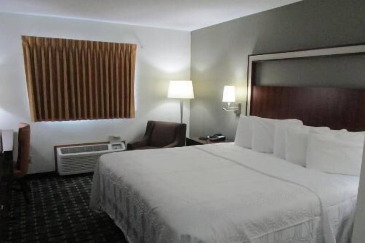 A hotel room with a bed, two bedside lamps, a chair, a desk, and a window with curtains.