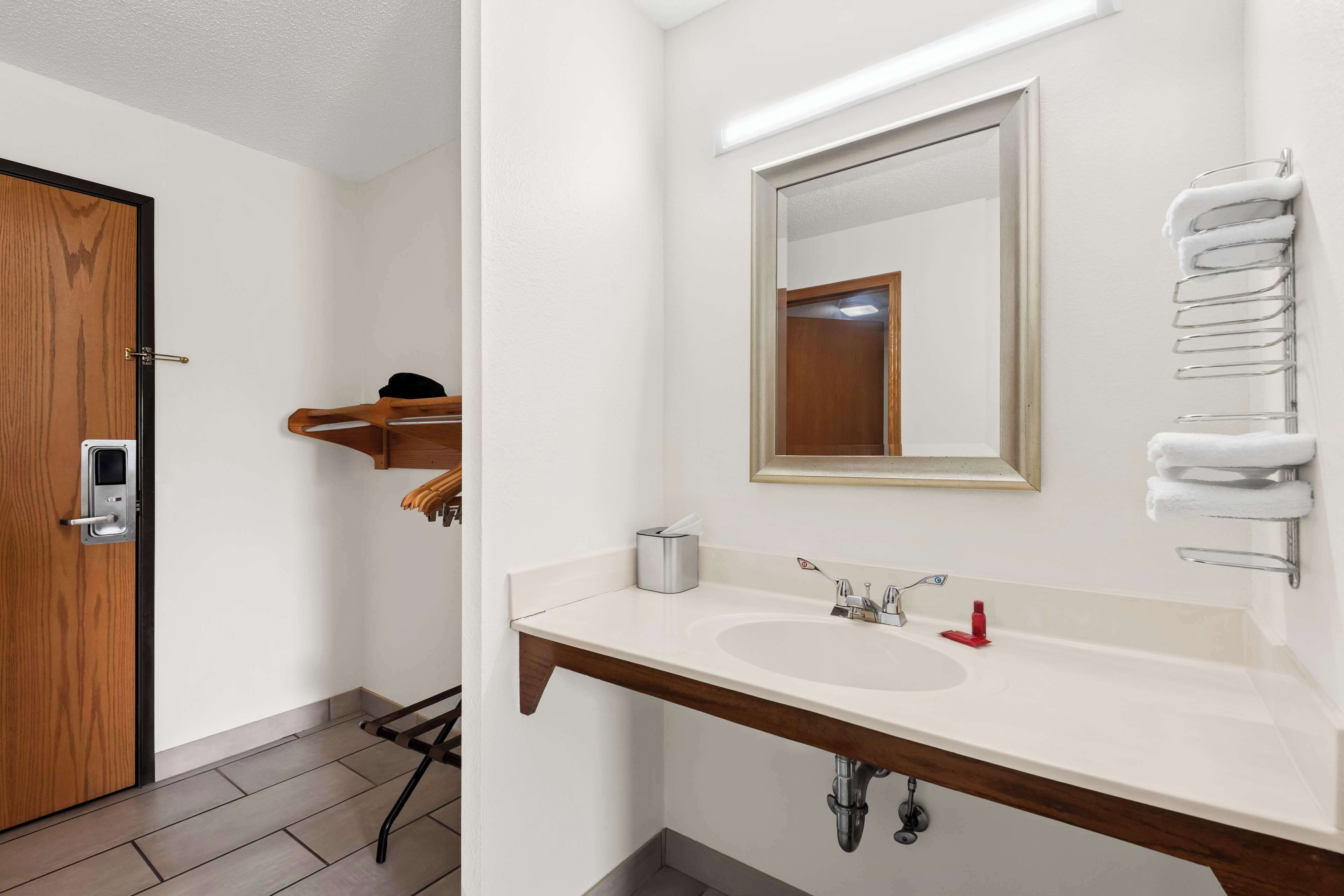 A modern bathroom with a wooden door, a white sink with a mirror above it, and a towel rack on the wall.
