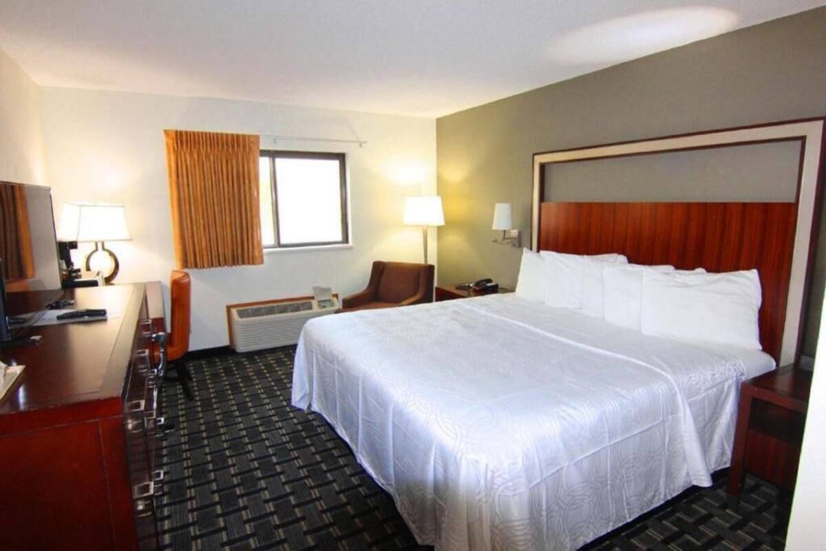 A hotel room with a large bed, a desk with a chair, a television, and a window with curtains.