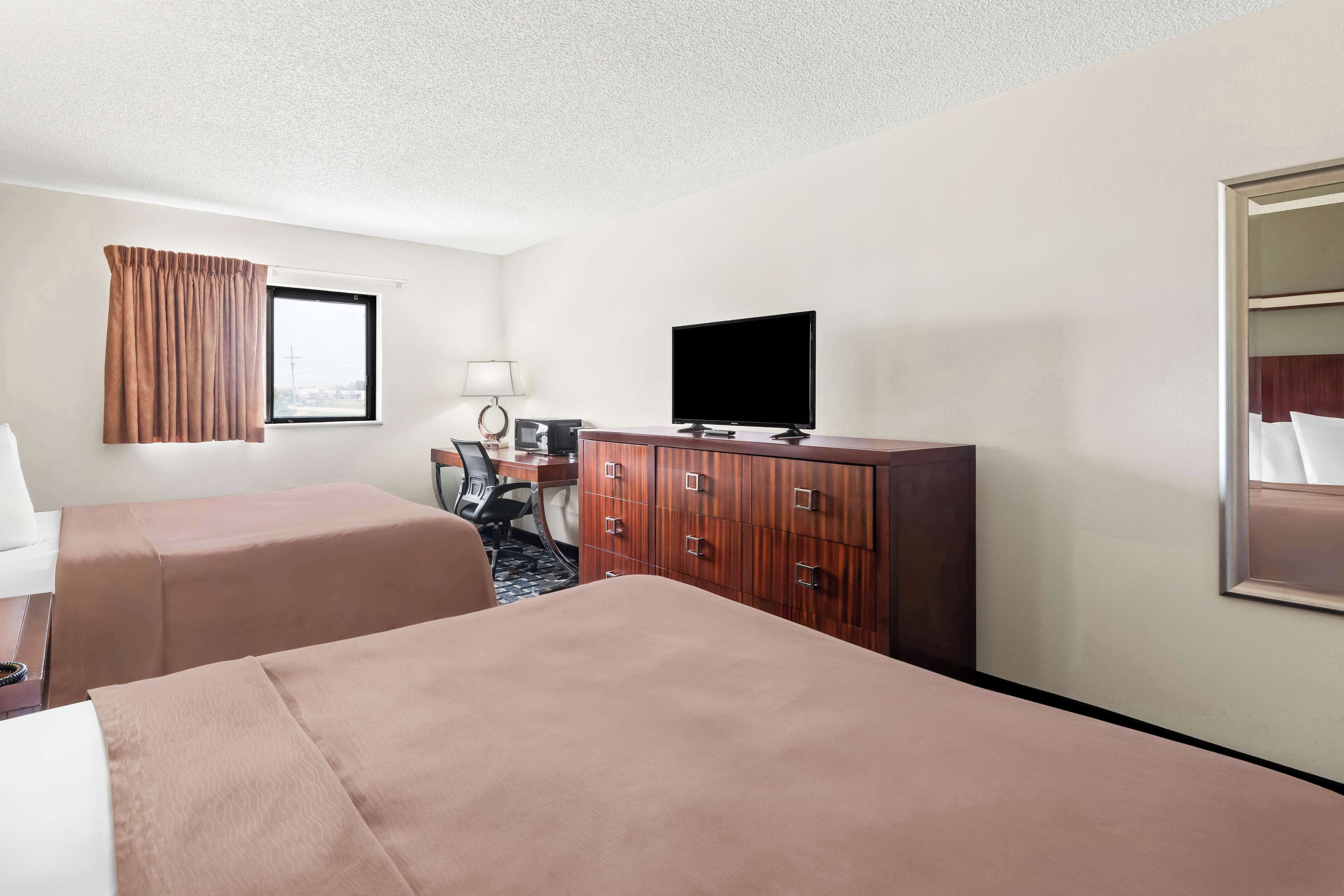 Une chambre d’hôtel avec deux lits, une télévision, un bureau avec une lampe et une armoire.