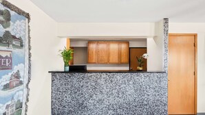 A reception area with a counter, wooden cabinets, a tiled wall, a door, and a poster on the wall. - SureStay Hotel by Best Western Manchester (Manchester)