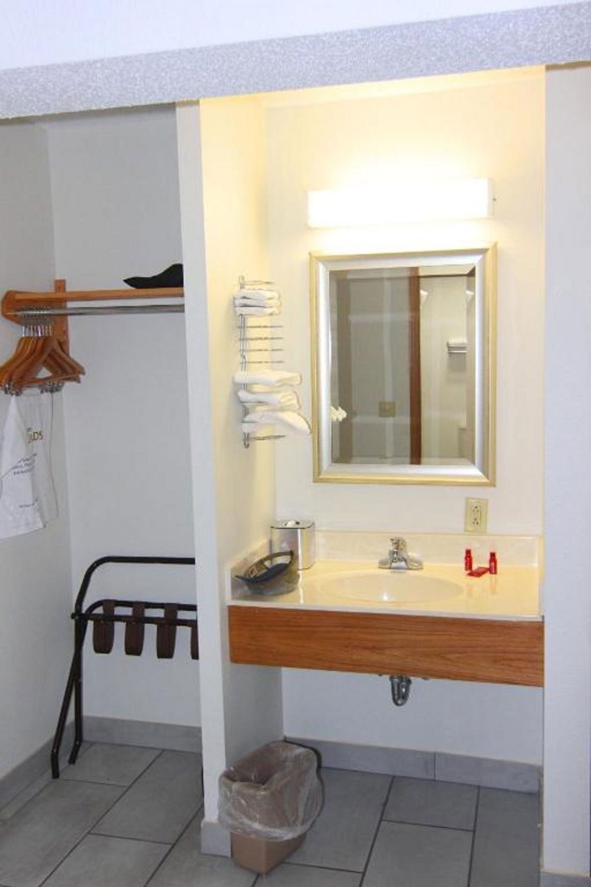 A bathroom with a wooden vanity, a mirror, a towel rack, and a trash bin.