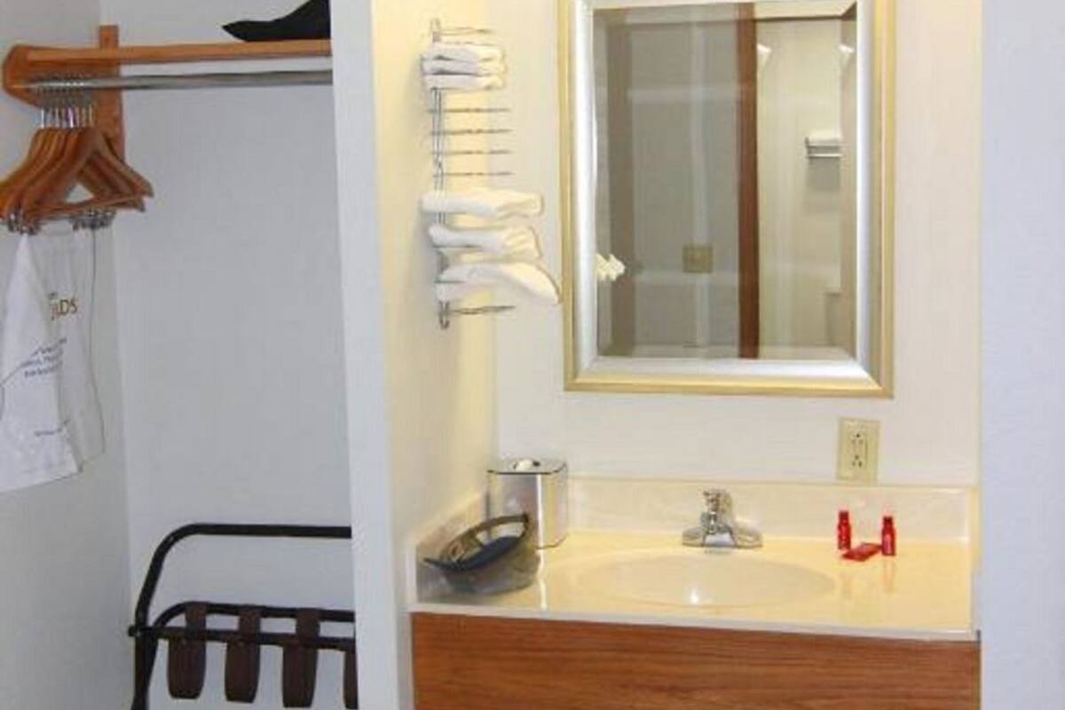 A bathroom with a wooden vanity, a mirror, a towel rack, and a trash bin.