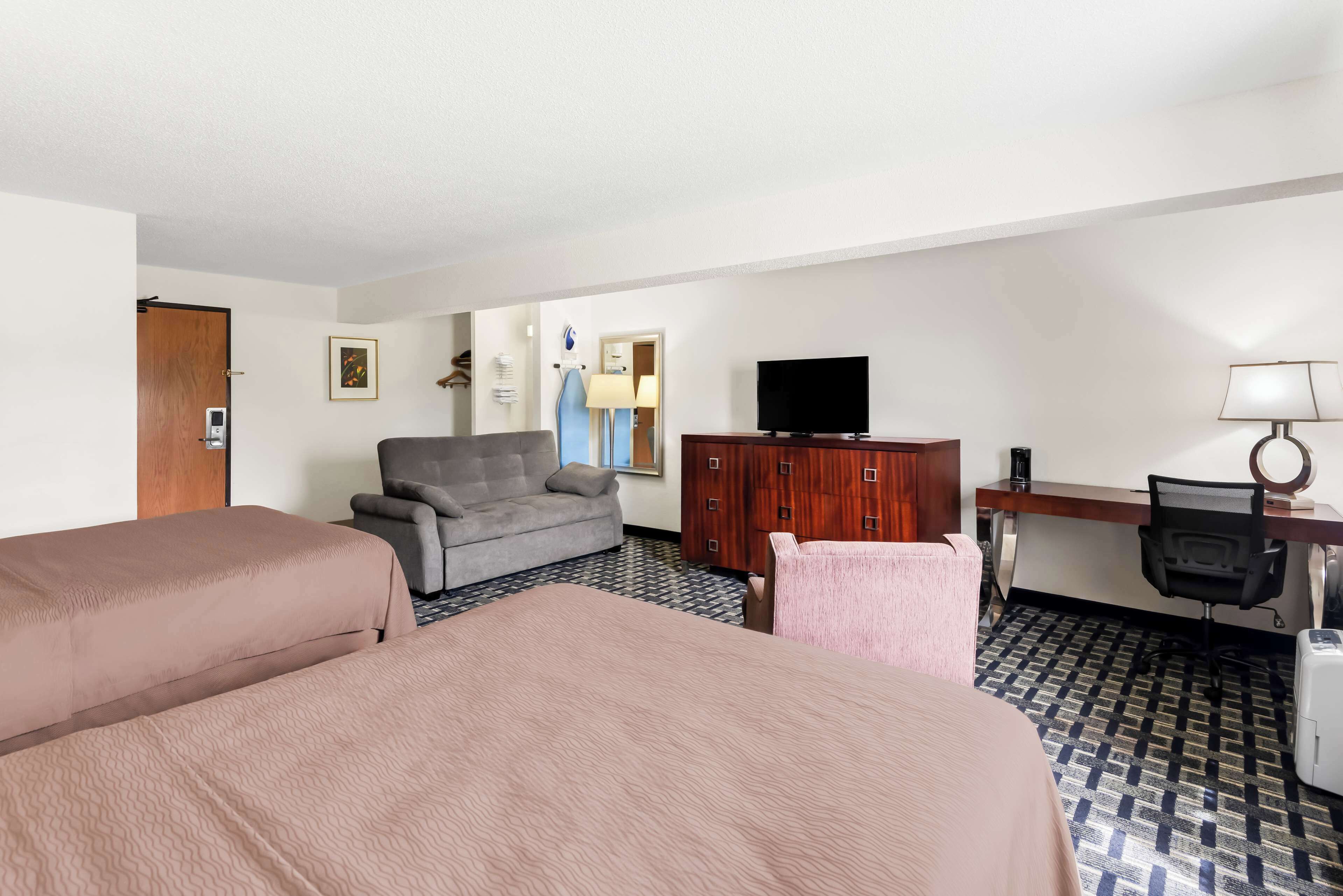 Une chambre d’hôtel avec deux lits, un canapé, une télévision, un bureau et une lampe.