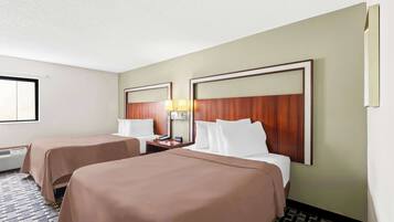 A hotel room with two beds, a nightstand with a lamp, and a window with blinds.