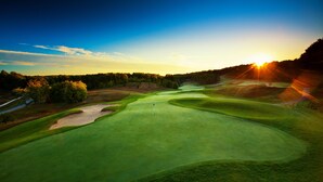 A golf course with a flagstick, sand bunkers, and a clear sky.