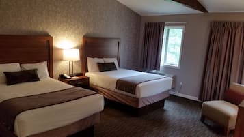 Una habitación de hotel con dos camas, una mesita de noche con lámpara, una ventana con cortinas y una silla.