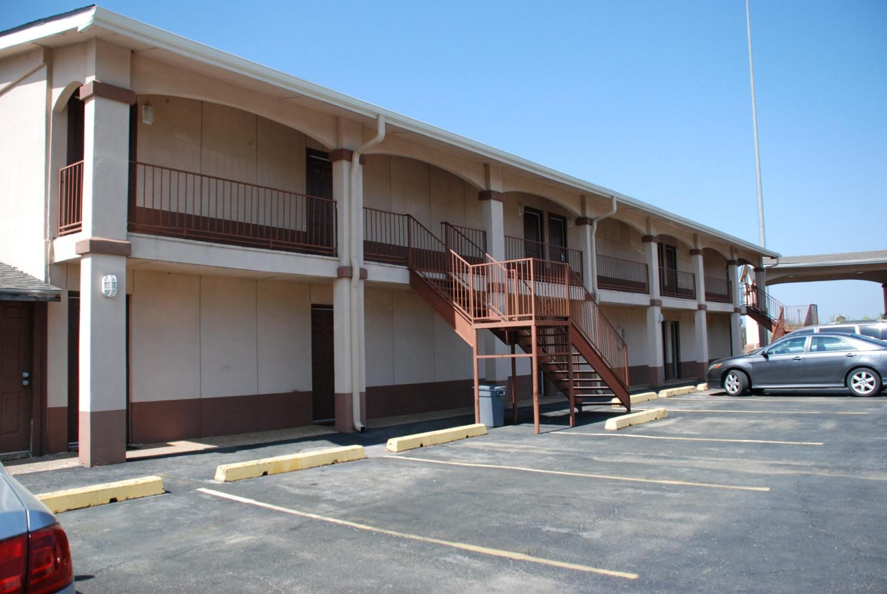 Un motel à deux étages avec un escalier central, un parking et une voiture garée devant.