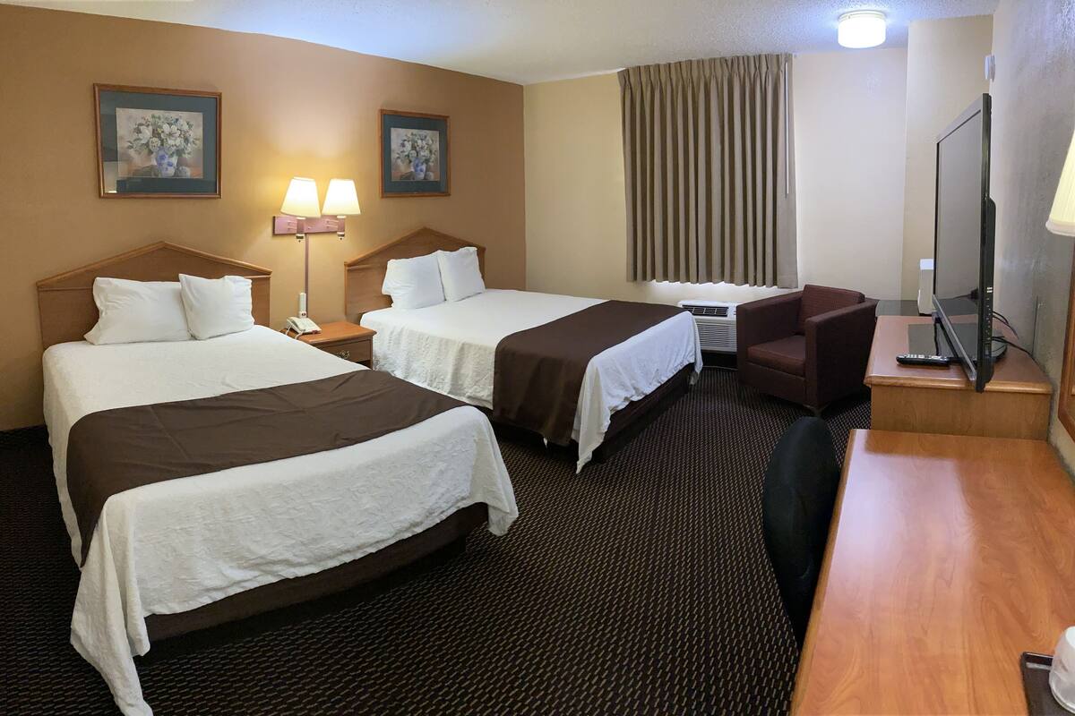 A hotel room with two beds, a desk with a chair, a TV, and a window with curtains.